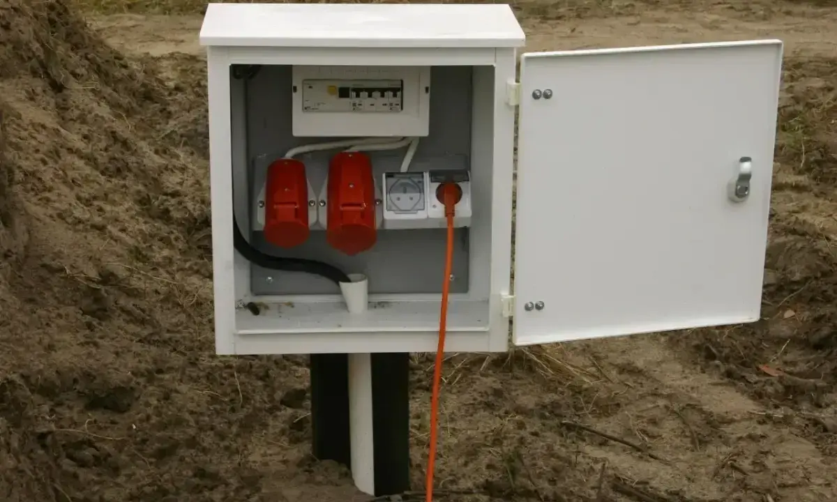 Skrzynka elektryczna na działce bez domu, gotowa do podłączenia prądu. Widoczne gniazda i zabezpieczenia.