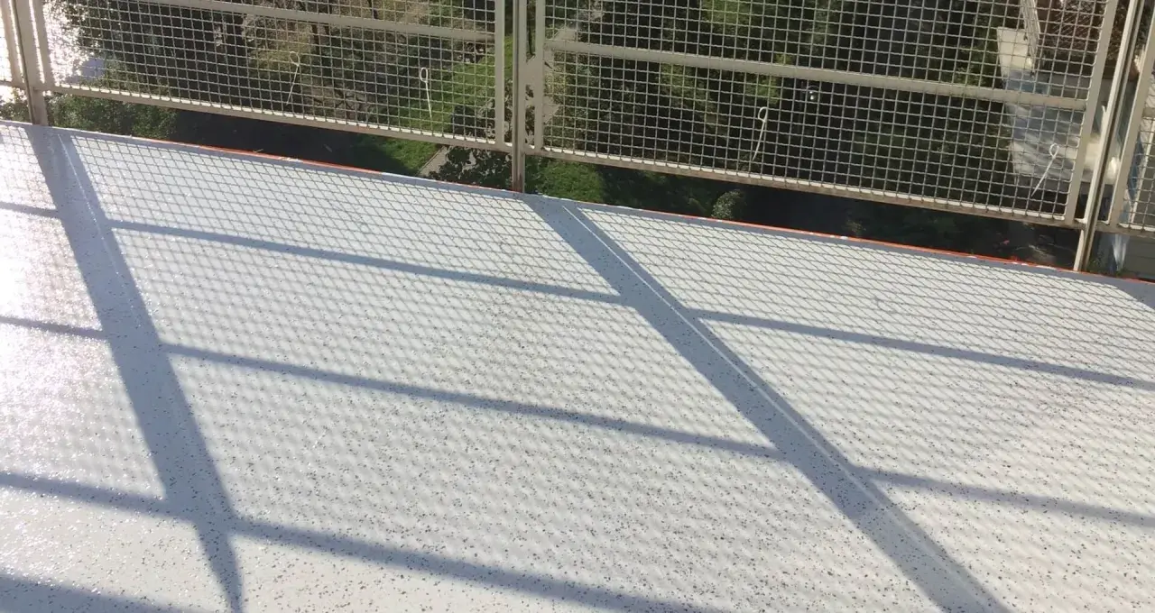 Nowy, biały balkon z żywicą, lśniący w słońcu. Cienie siatki tworzą ciekawy wzór na jego powierzchni.