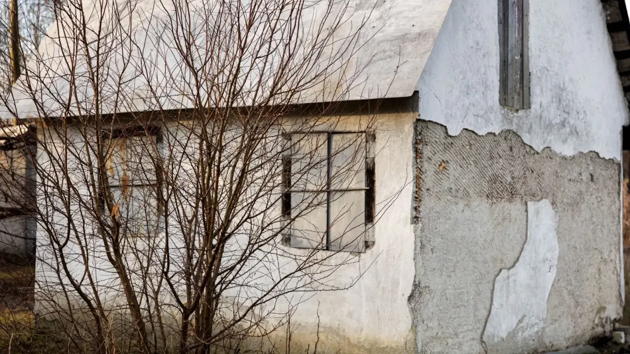 Elewacje starych domów: zniszczony tynk, puste okna i nagie gałęzie drzew tworzą melancholijną galerię.