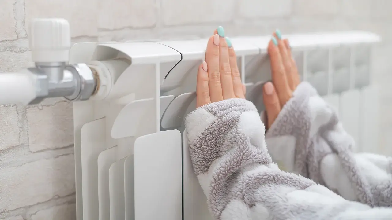 Dłonie ogrzewają się przy grzejniku, który ma podłączenie od dołu.