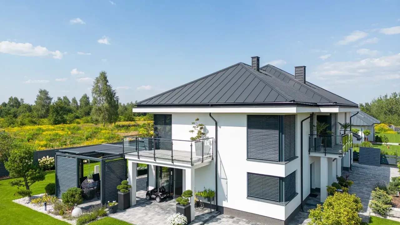 Nowoczesny dom z tarasem na dachu, otoczony zielonym ogrodem i polami kwitnących kwiatów.