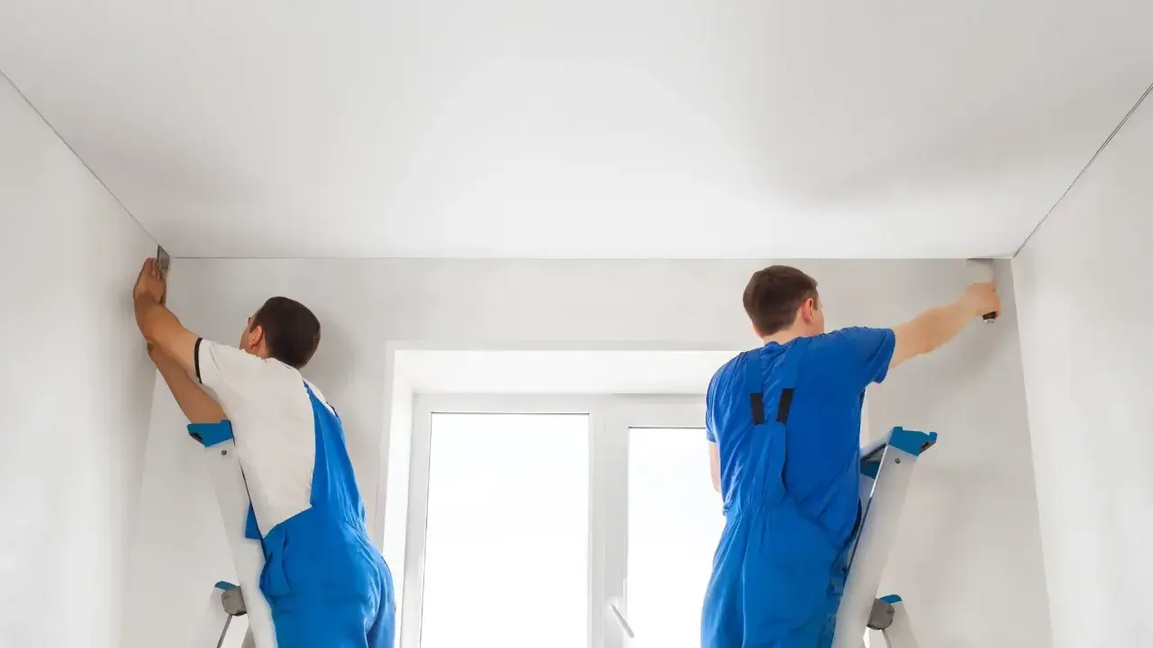 Dwóch fachowców montuje biały sufit napinany. Wzory na suficie są subtelne, tworząc gładką, jednolitą powierzchnię.