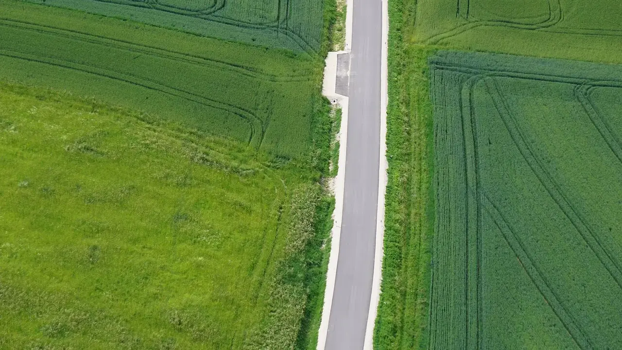 Asfaltowa droga dwukierunkowa przecina zielone pola. Minimalna szerokość drogi zapewnia płynny ruch.