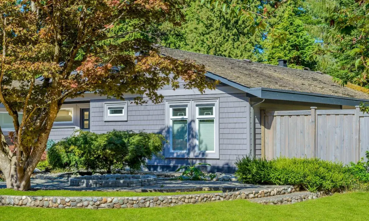 Szary bungalow z kamiennym murkiem i zadbanym ogrodem. To idealne miejsce na spokojne życie, czyli bungalow co to.