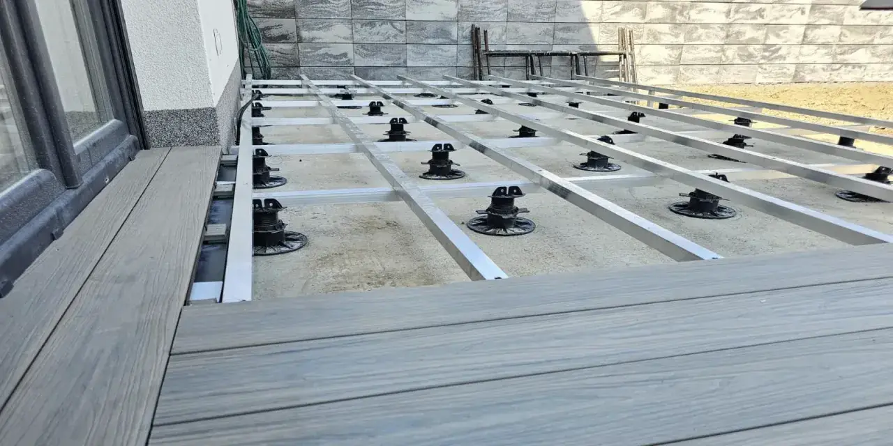 Budowa tarasu z deski kompozytowej. Widoczna konstrukcja nośna z aluminiowych profili i regulowanych podpór.