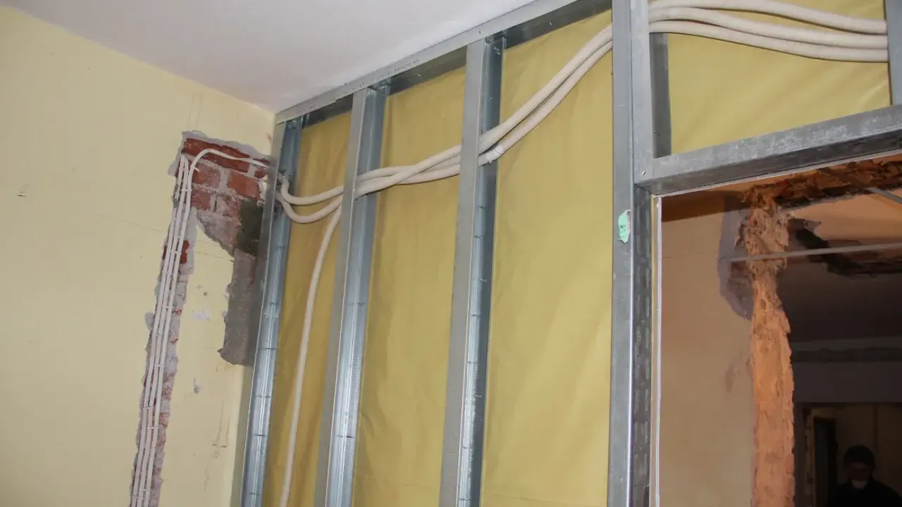 Trwa wymiana instalacji elektrycznej w mieszkaniu. Widać metalowy stelaż, żółtą membranę i nowe przewody elektryczne w peszlach.