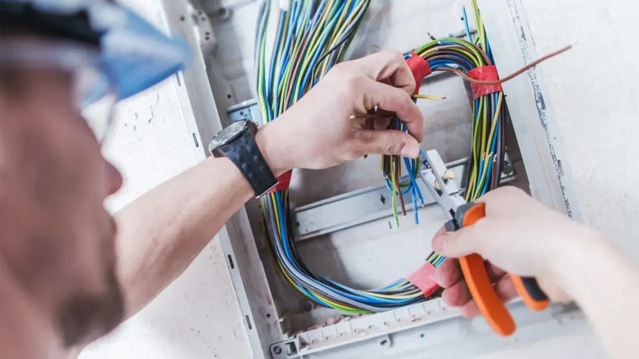 Elektryk pracuje nad prostą instalacją elektryczną, przycinając kolorowe przewody w skrzynce rozdzielczej.