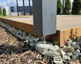 Solidny, podwyższony taras na gruncie, oparty na betonowych stopach i kamieniach. Drewniana konstrukcja z ciemnym słupkiem.