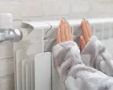 Dłonie ogrzewają się przy grzejniku, który ma podłączenie od dołu.