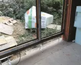 Próg drzwi tarasowych w trakcie montażu, przygotowany do ocieplenia progu. W tle materiały budowlane i zieleń.