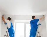 Dwóch fachowców montuje biały sufit napinany. Wzory na suficie są subtelne, tworząc gładką, jednolitą powierzchnię.