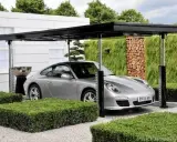 Srebrne Porsche pod nowoczesną wiatą, która może być częścią domu z garażem podziemnym.