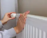 Ręka reguluje termostat grzejnika, przygotowując dom na zimę, kiedy zaczyna się sezon grzewczy.