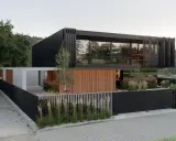 Piękne nowoczesne domy z czarną elewacją i drewnianymi akcentami, otoczone zielenią i nowoczesnym ogrodzeniem.