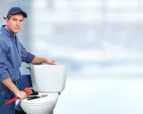 Hydraulik naprawia toaletę, bo spłuczka przepuszcza wodę. Narzędzia leżą na desce sedesowej.
