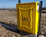 Żółta skrzynka gazowa z napisem "GAZ" przy ogrodzeniu. To element przyłącza gazu od skrzynki do domu.