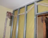 Trwa wymiana instalacji elektrycznej w mieszkaniu. Widać metalowy stelaż, żółtą membranę i nowe przewody elektryczne w peszlach.
