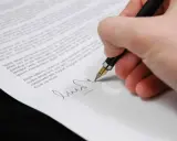 Podpisanie umowy przedwstępnej sprzedaży działki z zadatkiem. Dłoń z piórem składa podpis na dokumencie.