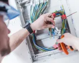 Elektryk pracuje nad prostą instalacją elektryczną, przycinając kolorowe przewody w skrzynce rozdzielczej.