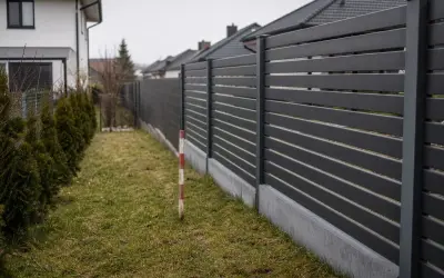 Nowoczesny, ciemnoszary płot oddziela posesje. Czy można postawić płot przy płocie sąsiada? Wąski pas trawy i żywopłot po lewej.