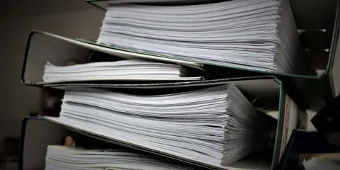 Stosy dokumentów w segregatorach. Czy wpis do księgi wieczystej jest obowiązkowy? Papiery czekają na uporządkowanie.