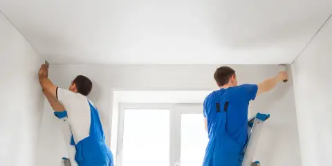Dwóch fachowców montuje biały sufit napinany. Wzory na suficie są subtelne, tworząc gładką, jednolitą powierzchnię.