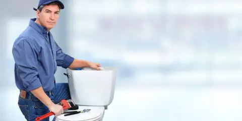 Hydraulik naprawia toaletę, bo spłuczka przepuszcza wodę. Narzędzia leżą na desce sedesowej.