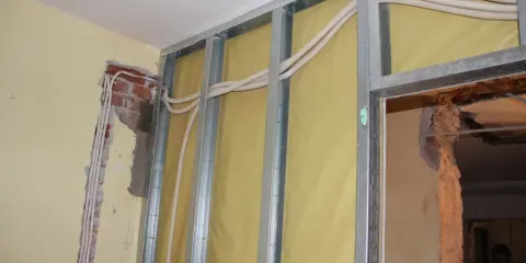 Trwa wymiana instalacji elektrycznej w mieszkaniu. Widać metalowy stelaż, żółtą membranę i nowe przewody elektryczne w peszlach.