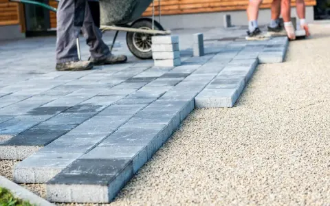 Układanie betonowych płyt na żwirze. Pracownicy tworzą nowoczesny taras, gdzie beton zamiast kostki brukowej stanowi estetyczne i trwałe rozwiązanie.