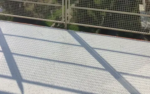 Nowy, biały balkon z żywicą, lśniący w słońcu. Cienie siatki tworzą ciekawy wzór na jego powierzchni.
