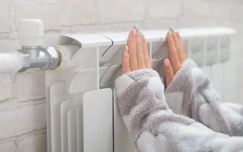 Dłonie ogrzewają się przy grzejniku, który ma podłączenie od dołu.