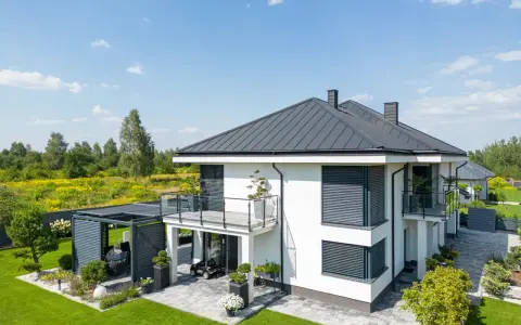 Nowoczesny dom z tarasem na dachu, otoczony zielonym ogrodem i polami kwitnących kwiatów.