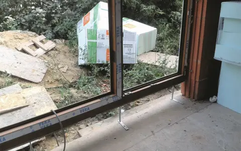 Próg drzwi tarasowych w trakcie montażu, przygotowany do ocieplenia progu. W tle materiały budowlane i zieleń.