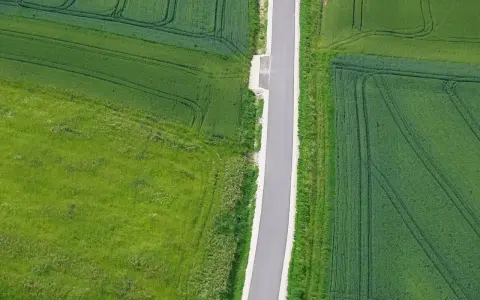 Asfaltowa droga dwukierunkowa przecina zielone pola. Minimalna szerokość drogi zapewnia płynny ruch.