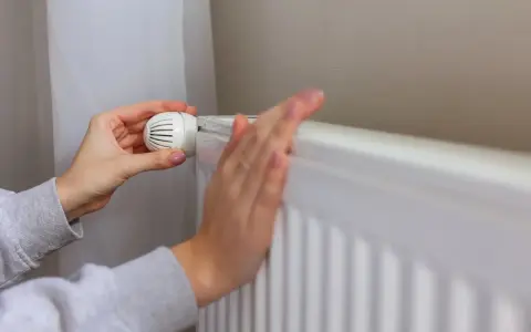 Ręka reguluje termostat grzejnika, przygotowując dom na zimę, kiedy zaczyna się sezon grzewczy.