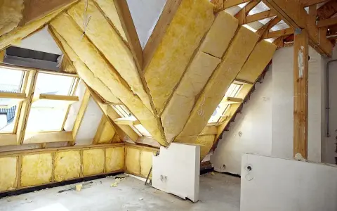 Widok na poddasze w trakcie prac. Drewniana konstrukcja dachu, okna dachowe i żółta wełna mineralna świadczą o postępie prac nad adaptacją poddasza. Projekt w toku.