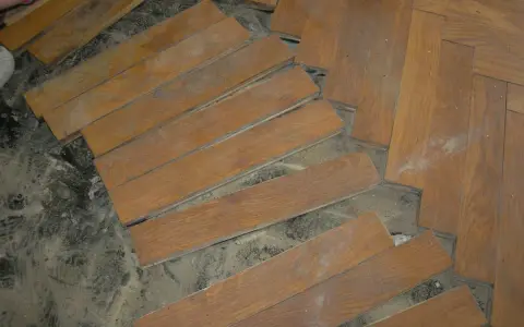 Drewniana podłoga w jodełkę, częściowo rozebrana. Widać pojedyncze deseczki i fragmenty ułożenia. Czy to subit?