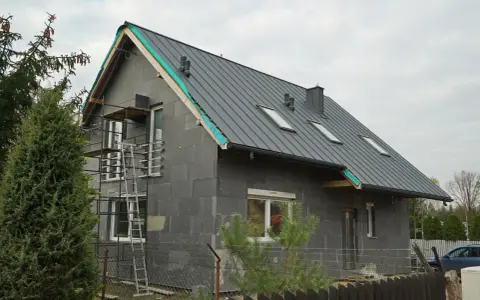 Przebudowa starego domu projekty: szary dom w trakcie budowy, z nowym dachem, oknami i rusztowaniami.