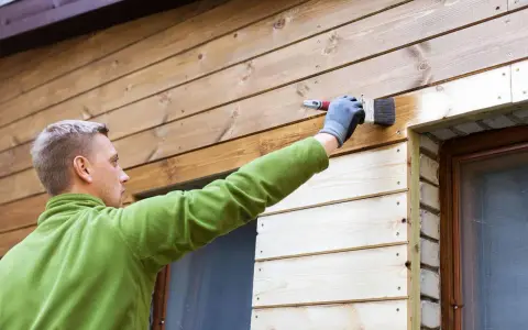 Mężczyzna maluje deskę elewacyjną, tworząc piękne aranżacje drewnianego domu.