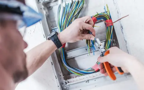 Elektryk pracuje nad prostą instalacją elektryczną, przycinając kolorowe przewody w skrzynce rozdzielczej.