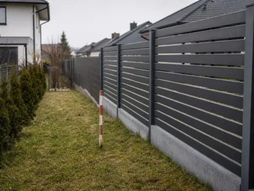 Nowoczesny, ciemnoszary płot oddziela posesje. Czy można postawić płot przy płocie sąsiada? Wąski pas trawy i żywopłot po lewej.