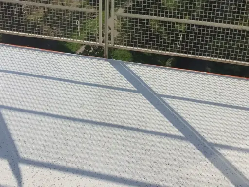 Nowy, biały balkon z żywicą, lśniący w słońcu. Cienie siatki tworzą ciekawy wzór na jego powierzchni.