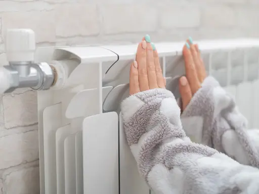Dłonie ogrzewają się przy grzejniku, który ma podłączenie od dołu.
