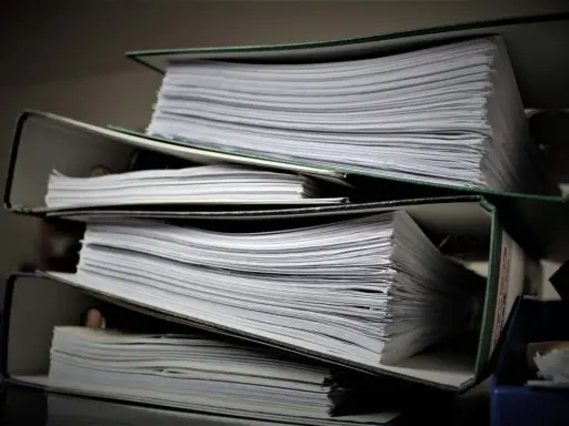 Stosy dokumentów w segregatorach. Czy wpis do księgi wieczystej jest obowiązkowy? Papiery czekają na uporządkowanie.