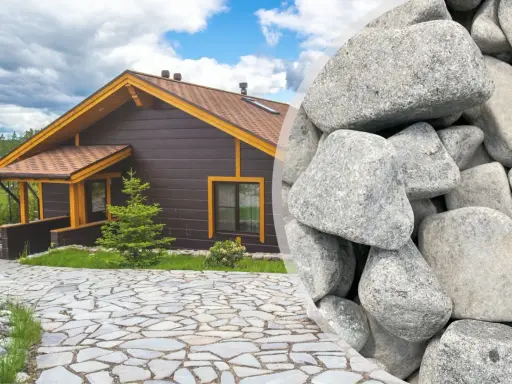 Elegancki podjazd z kamienia prowadzi do przytulnego drewnianego domu. Obok widać stos dużych, szarych kamieni, idealnych do stworzenia podobnej nawierzchni.