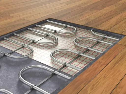 Instalacja ogrzewania podłogowego wodnego pod drewnianą podłogą. Metalowe rurki ułożone na siatce izolacyjnej.