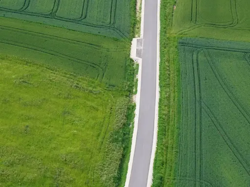 Asfaltowa droga dwukierunkowa przecina zielone pola. Minimalna szerokość drogi zapewnia płynny ruch.
