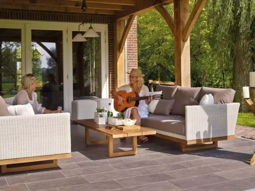 Kobieta gra na gitarze na tarasie, siedząc na sofie obok koleżanki. To idealne miejsce na relaks, jakby to był prywatny balkon.