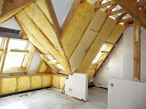 Widok na poddasze w trakcie prac. Drewniana konstrukcja dachu, okna dachowe i żółta wełna mineralna świadczą o postępie prac nad adaptacją poddasza. Projekt w toku.