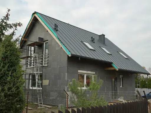 Przebudowa starego domu projekty: szary dom w trakcie budowy, z nowym dachem, oknami i rusztowaniami.